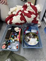 Red and white patterned quilt with two plastic bins containing various sewing supplies such as thread spools, buttons, and scissors.