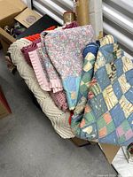 Box of folded handmade quilts and afghans showing patchwork and crochet pieces in soft colors.