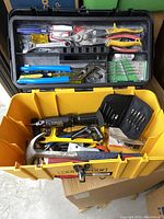 Open yellow plastic toolbox filled with various hand tools and tool accessories organized in the top tray and main compartment.