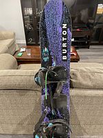 Full view of Burton snowboard showing graphic design combining black and purple splattered pattern with black bindings fixed.