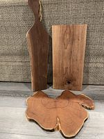 Photo of three different wooden charcuterie boards: one large round slab with visible wood rings and living edge; one rectangular smooth board with wood knots; one paddle shape board with rope handle.