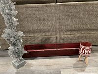 Photo showing silver artificial Christmas tree standing next to long red wooden centerpiece box on floor