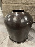 Close-up photo of a dark round metal vase with a wide opening, displaying its shape and texture.