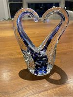Front view of hand blown open heart glass sculpture with embedded bubbles and blue accent, placed on wooden surface.