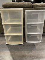 Two plastic drawer storage bins side by side against a couch; beige 3-drawer bin on the left and white 2-drawer bin on the right.