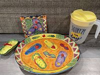 Set of ceramic summer-themed serving pieces and plastic pitcher arranged on couch.