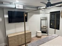 Wall-mounted flat screen TV in a modern bedroom with dresser, mirror, and ceiling fan visible