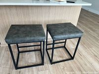 Two grey PU leather padded backless bar stools with black chromed metal frames place in front of kitchen island counter.