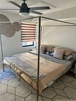 Photo of a king size gold metal canopy bed frame with modern design, set up in a room with bedding for scale.