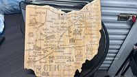 Photo of bamboo wooden cutting and serving board shaped like Ohio with engraved city and town names.