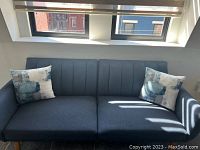 Photo of navy blue Novogratz Brittany sofa futon in daylight with two patterned cushions on either side.