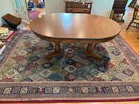 Full view of the area rug under a wooden dining table on a hardwood floor showing the geometric diamond pattern and floral border.