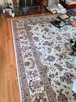 Full view of the floral patterned cream area rug spread on hardwood floor showing overall condition and pattern details.