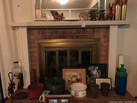 Full view of fireplace mantel and hearth showing woven baskets, framed art prints, ceramic jar and pots, vintage bottle, and candleholders