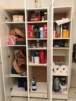 White shelving unit with woven baskets, cleaning sprays, paper towels, and storage tins