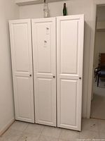 Front view of three tall white cabinets with paneled doors standing side by side.