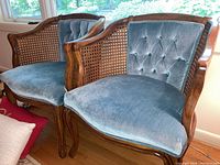 Pair of blue velvet upholstered armchairs with cane sides, wooden frames, and carved legs