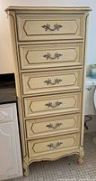 Front view of the cream-colored French Provincial style chest of drawers showing six drawers with decorative handles.