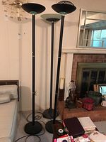 Three black metal floor lamps standing side by side near a fireplace, showing their full height and bases.