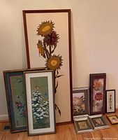 Framed yarn art sunflower with multiple sunflowers on beige background with wood frame, surrounded by various smaller framed Asian print art and needlepoint pieces.