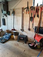 Wide view of gardening tools hanging on wall, flower pots, baskets, step stool, and toolbox on floor