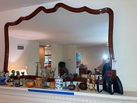 Front view of large rectangular wall mirror with carved wooden frame and scalloped top edge, reflecting room interior.
