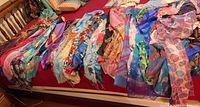 Multiple colorful scarves laid out on a bed showing a variety of floral, abstract, and striped patterns in various colors and textures.