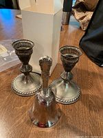 Photo of two matching sterling silver candle sticks and one ceremonial bell placed on a wooden surface showing overall condition and appearance.