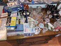 Overview of assortment of tea lights, candle holders, candles, and snuffers arranged on a table showing glass, black metal items, boxed candles, and a birthday candle holder.
