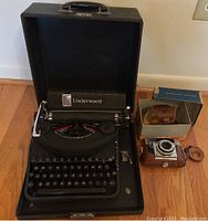 Overview photo showing the Underwood typewriter in its black carrying case and the Agfa Optima III S camera with its box and leather case on the floor.
