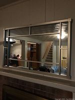 Front view of large rectangular wall mirror mounted above a brick surface showing segmented panels formed by metal bars in a silver frame.