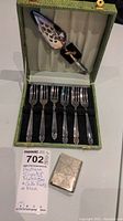 Full view of the antique matchbox, cake forks, and pierced cake server arranged in green lined box
