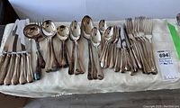 Full display of cutlery including knives, forks, large and small spoons and serving pieces on white cloth.