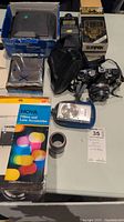 Photo showing Polaroid ProCam in box, Sunpak flash box, Canon PowerShot digital camera accessories, lens, and film packs.