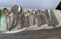Photo showing full cutlery set laid out on cloth including forks, knives, spoons and serving pieces all with ornate patterned handles.