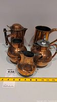 Five copper jugs arranged on a table showing their varying sizes and shapes