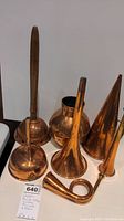 Various copper items including clothes washer, funnels, pitcher and horn arranged on a white surface
