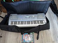 Yamaha electric keyboard inside open soft carrying case with instruction materials beneath it.