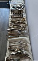 Photo showing the full collection of cutlery laid out, including forks, knives, spoons and an electroplated napkin holder.