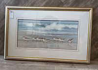 Photo of entire framed art print showing the beach scene with shorebirds and waves. Frame is gold with silver tones, matting around the print is cream.