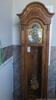 Full front view of the tall grandfather clock showing the curved top, clock face, wooden case and base.