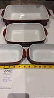 Top view showing all four rectangular ceramic bakeware dishes in red with white interiors and handles, measuring tape included for size reference.
