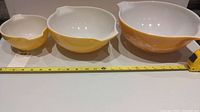 Three yellow Pyrex mixing bowls showing size comparison with measuring tape