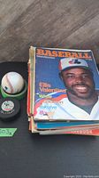 Signed baseball on green stand and signed hockey puck with stack of vintage baseball magazines including Baseball magazine with Ellis Valentine on the cover.