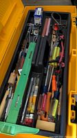 Open yellow toolbox showing assorted hand tools inside including screwdrivers, pliers, and other small tools.