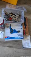 Plastic container with assorted metal hand tools including clamps and pliers; boxed Mastercraft cordless drill; boxed Ryobi oscillating multi-tool; instruction manual lying beside items on floor