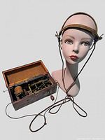 Wooden box opened with visible internal hand crank mechanism and head harness accessory beside it.