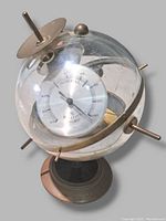 Clear view of the antique weather meter showing glass globe with dial face, metal rotating mechanism inside, and crack at bottom