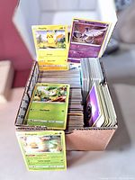 Box filled with Pokémon trading cards with visible Pikachu, Genus Articuno, Pedal, Eldeross cards on display.