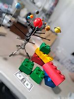 Photo showing large rubber LEGOLAND bricks in various colors with a metal and plastic solar system model including multiple planets on arms, a one-dollar bill for scale.